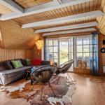 Living room with wooden ceiling, sofa, chairs, and windows to terrace.