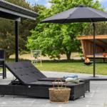 Terrace with lounge chair, umbrella, and fire pit. Background: lawn, tree, and trampoline.