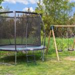 A trampoline with safety net and a swing in the garden.