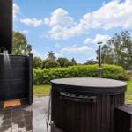 Outdoor hot tub with shower and grill, surrounded by greenery and trees.