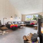 Living room with wooden walls, sofa, chair, and wood stove. Window with view outside.