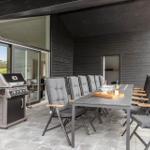 Terrace with grill, dining table, and chairs. Background: house with glass facade.