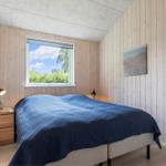 Bedroom with wooden walls, bed with blue blanket, and window with view of trees.