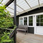 Terrasse mit Sitzbank, weiße Tür und Fenster, schwarz verputzte Wand, Glasdach, grüne Pflanzen