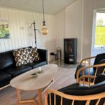 Wohnzimmer mit Sofa, zwei Stühlen, Tisch und Kaminofen. Fenster mit Blick auf Grünfläche.