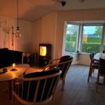 Wohn- und Essbereich mit Kamin, Holzfußboden und großem Fenster zur grünen Außenansicht.