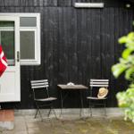 Backyard with table, two chairs, and Danish flag in front of black wooden house.