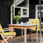 Bright green seating surrounds a wooden table on a terrace in front of a black-clad house.