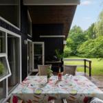 Deck with table, chairs, and grill. View of green lawn and trees.