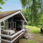 House with terrace, table and chairs, surrounded by greenery and trees.