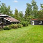 Black wooden house with terrace and large lawn in greenery.
