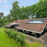Black house with solar panels, terrace, and green garden. Surrounded by trees.