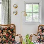 Zwei Rattan-Stühle mit floralen Bezügen stehen vor einem Fenster mit grünem Blick.