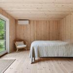 Schlafzimmer mit Holzwand, Bett, Stuhl und Fenster zur Außenseite.