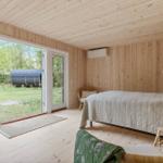Schlafzimmer mit Holzwand, Bett, Stehlampe und Terrassentür zur Grünfläche.