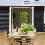 Terrasse mit Esstisch, Stühlen und Blumen vor schwarzem Holzhaus mit offenen Türen.