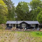 Schwarze Holzhütte mit Terrasse, Garten und umgeben von Bäumen.