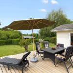 Deck with table, chairs, lounge chair, and umbrella. Background: green garden and house.