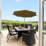 Terrace with table, chairs, and umbrella. View of green meadows and trees.