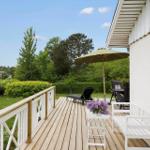 Deck with lounge chair, umbrella, and white bench. View of green lawn and trees.