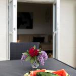 Table with watermelon and flowers in front of open door to living area.