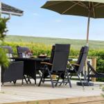 Terrace with table, chairs, and umbrella. Green background with hedges.