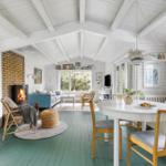 A room with green floor, white ceiling, and wooden furniture. It has a fireplace, a table, and windows.