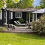 Black wooden house with terrace, sun loungers, and umbrella. Surrounded by greenery.