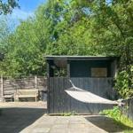 Hammock seating area in front of a wooden shed with garden and trees.