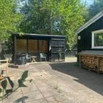 Backyard with pavilion, seating, and firewood stack beside a black house.