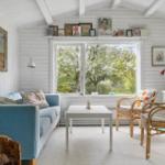 A living room with a blue sofa, two rattan chairs, and a large window overlooking trees.