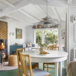 A room with dining area, sofa, and fireplace. Wooden ceiling, white walls, and green floor.
