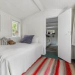 Bedroom with white bed, striped rug, and view into the kitchen.