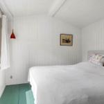 Bedroom with white panel walls, bed, and window with view outside.
