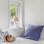 A bed with pillows and a hat by a window with a view of green.