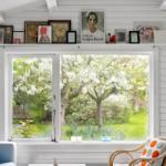 A room with white wood paneling, large window, and view of blooming trees. Candles sit on the sill.