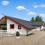 A white holiday home with a red roof and terrace under a blue sky.