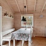 Wooden house with kitchen, dining table, and seating. White furniture and windows.
