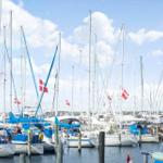 Sailboats with masts and Danish flags are docked. Blue sky with white clouds.