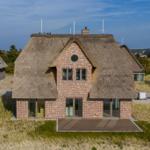 Haus mit Strohdach und Backsteinfassade auf Dünenlage