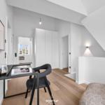 Schlafzimmer mit Schreibtisch, Bett und Kleiderschrank unter Dachschrägen.