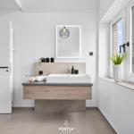 Badezimmer mit Waschtisch, Spiegel und Fenster mit Pflanze.