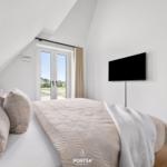 Schlafzimmer mit Dachbodenfenster, Bett und Wandfernseher.
