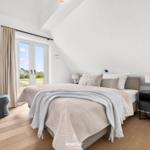 Schlafzimmer mit Doppelbett, Fenster und Holzboden.