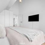 Schlafzimmer mit Bett, Kleiderschrank und Wand-TV. Dachschrägen und Holzboden.