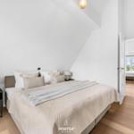Schlafzimmer mit Bett, Nachttischen und Holzboden. Tür führt in einen weiteren Raum.