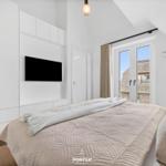 Schlafzimmer mit Bett, TV und Fenster mit Blick auf Dächer.
