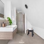 Badezimmer mit Dusche, Waschbecken und Spiegel. Dachneigung sichtbar.