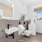 Badezimmer mit Waschbecken, WC und Waschmaschine. Fenster mit Blick nach draußen.