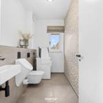 Moderne Badezimmer mit Waschbecken, WC und Fenster. Wandverkleidung und Spiegel mit Beleuchtung.